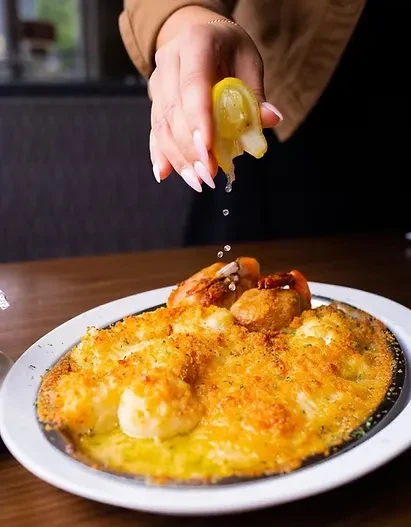 A hand squeezes lemon over a golden-brown seafood gratin.