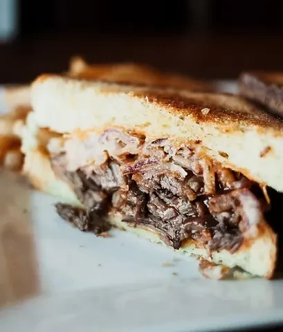 Cross-section of a toasted sandwich with dark shredded meat and light toppings.
