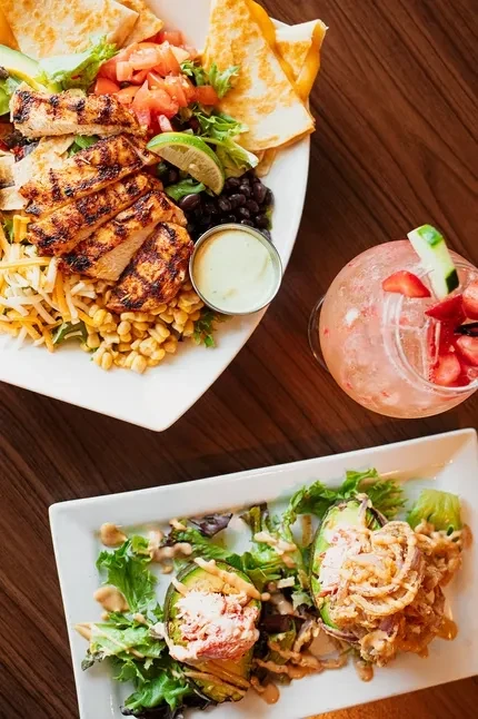 Overhead view of chicken salad, pink cocktail, and avocado appetizer.
