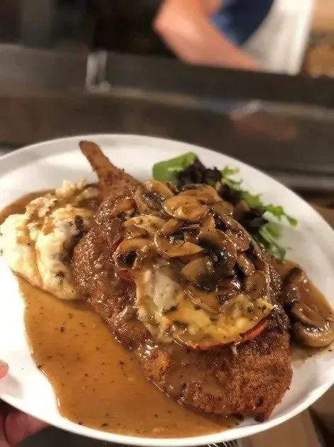 Breaded cutlet with gravy, mushrooms, cheese, mashed potatoes, and salad.