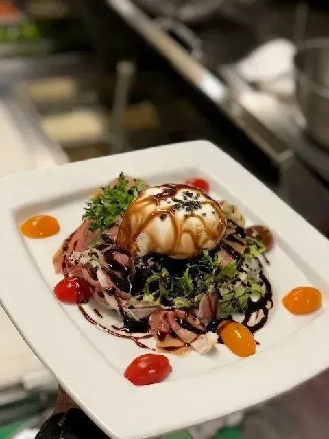 Artfully plated burrata salad with prosciutto, tomatoes, and balsamic.