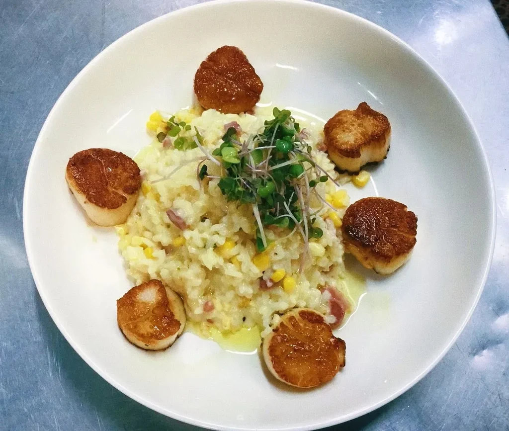 Seven seared scallops with creamy corn and ham risotto, microgreens.
