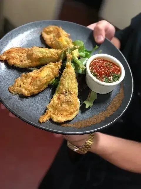 Crispy fried zucchini flowers, red sauce, on a dark plate.