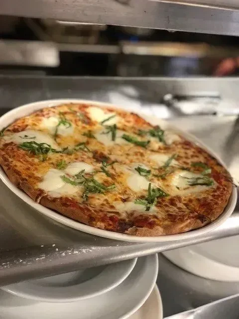 Golden-crusted Margherita pizza on an oval dish in a dim kitchen.