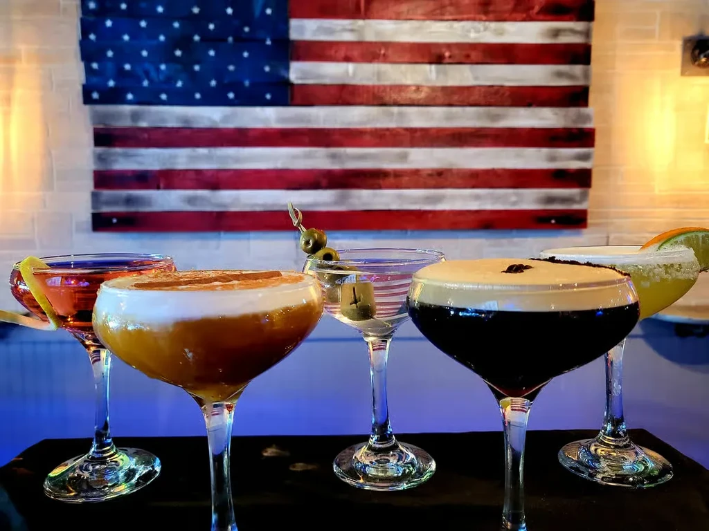 Five distinct cocktails on a bar, rustic American flag background.