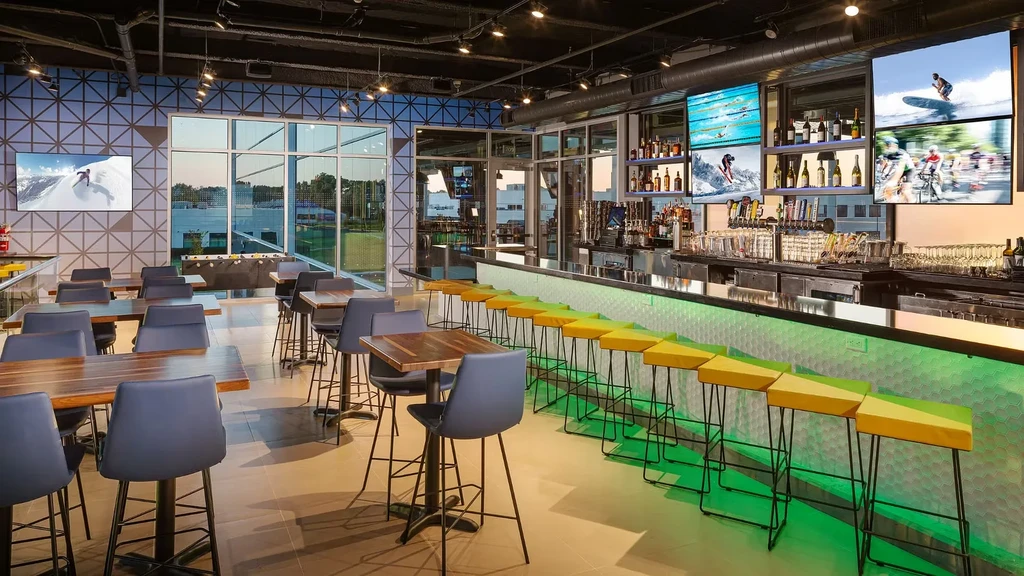 Modern, empty sports bar with vibrant green-lit bar and sports TVs.