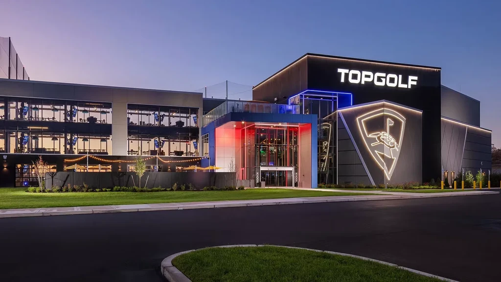 Illuminated TOPGOLF building at dusk, showing golf bays and patio.
