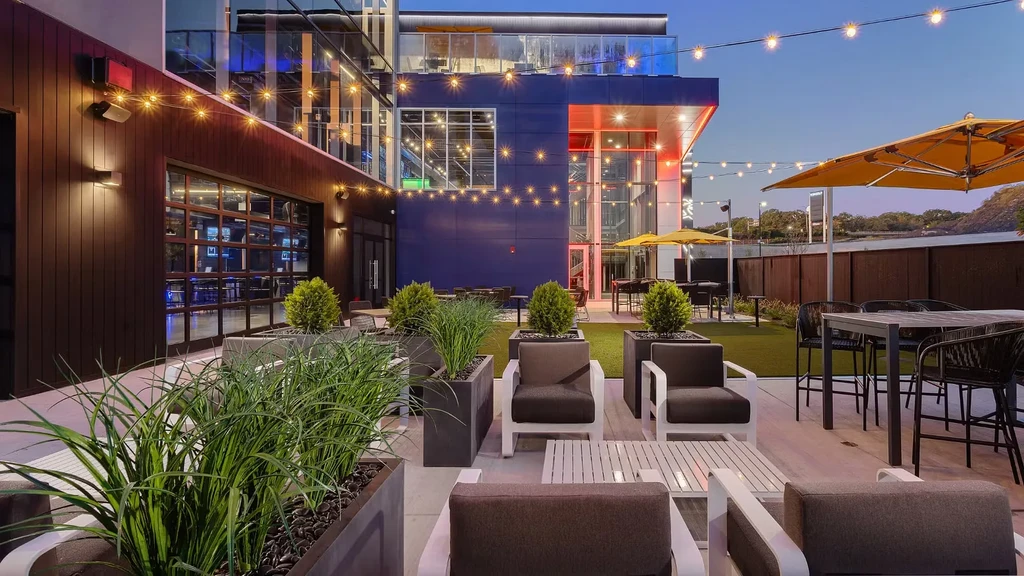 Modern outdoor restaurant patio at dusk with string lights and blue building.