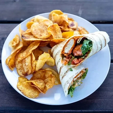 Grilled chicken wrap halves, greens, tomatoes, and crispy potato chips.