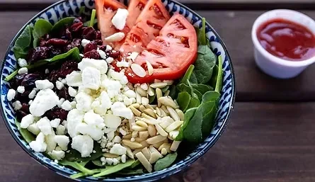 Spinach salad with feta, cranberries, tomatoes, and almonds in a patterned bowl.