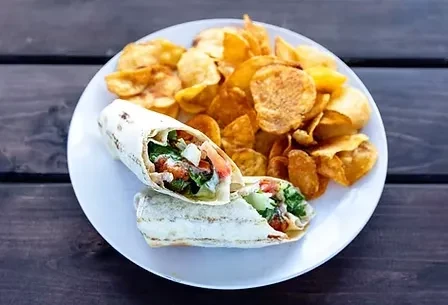 Grilled wrap with green vegetables and chips on a wooden table.