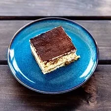 Layered tiramisu with cocoa on a blue plate, dark wood background.