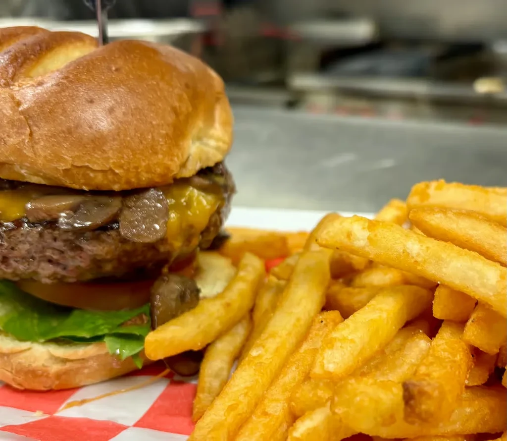 Mushroom cheeseburger with melted cheese, golden fries, on checkered paper.
