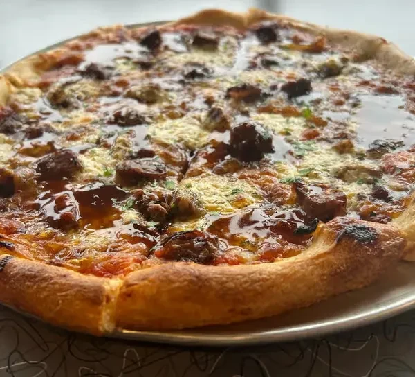 Meat pizza with melted cheese, tomato sauce, drizzled glaze, and herbs.