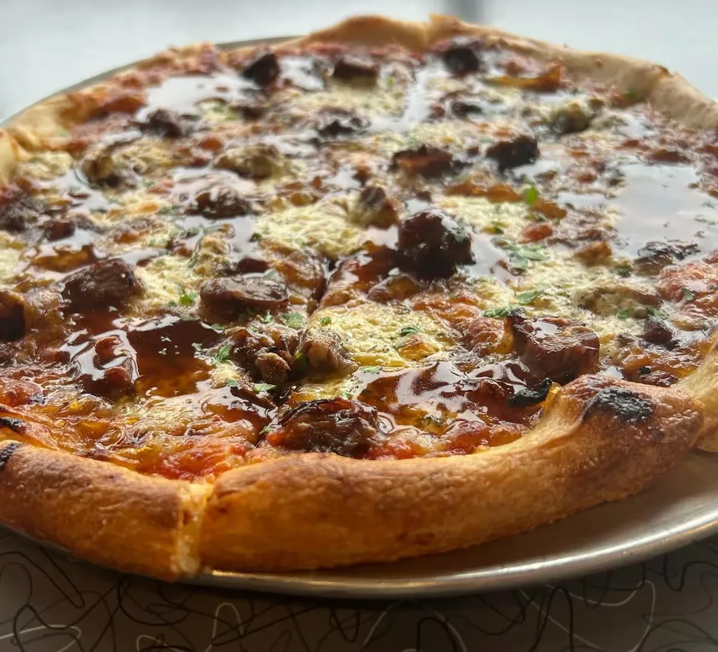 Whole pizza with meat, melted cheese, dark drizzle, and green herbs.