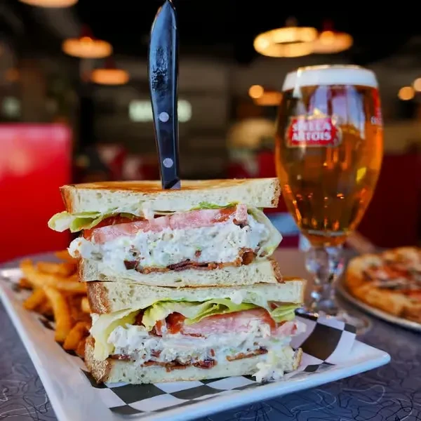 Close-up of stacked bacon sandwich, fries, and Stella Artois beer.