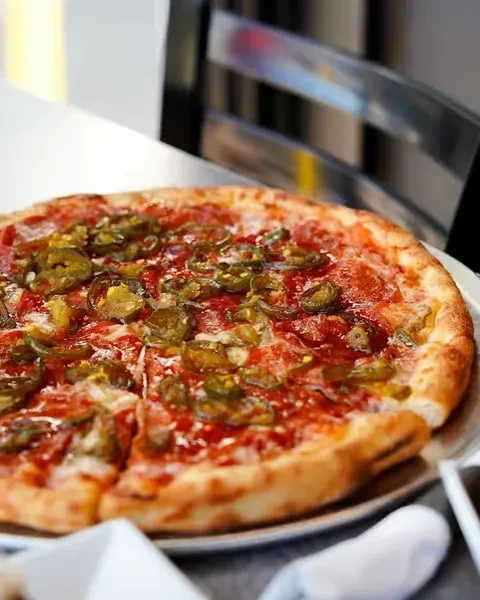A partially sliced pepperoni and jalapeño pizza on a metal tray.