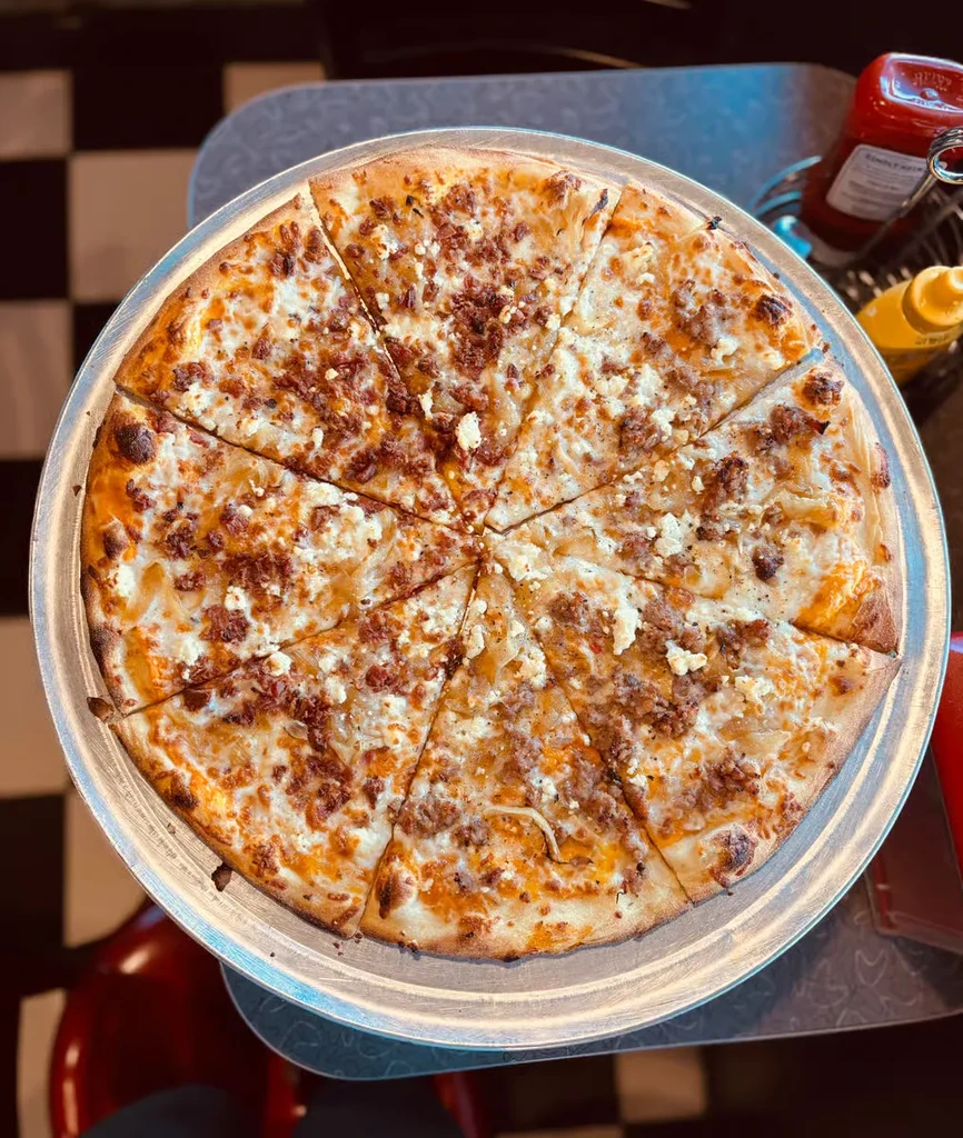 Overhead view of pre-cut pizza with cheese, sausage, on a metallic pan.