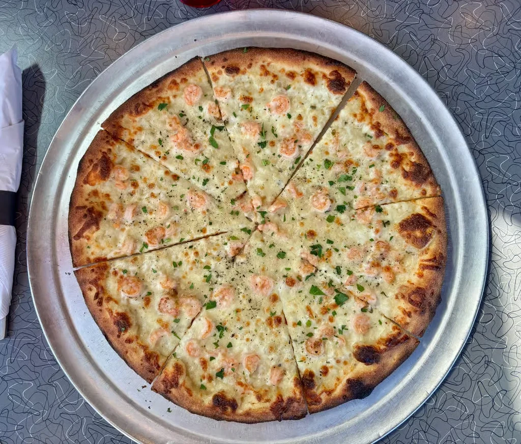 Top-down shrimp pizza with white sauce, herbs, on silver tray.