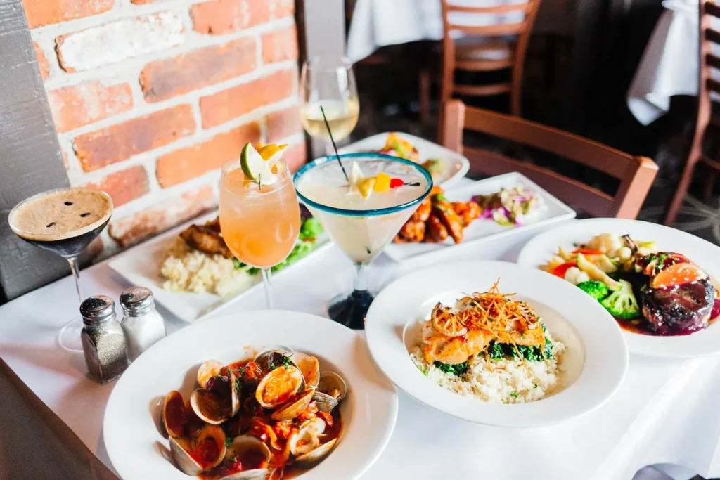 Restaurant table with multiple plated dishes and colorful cocktails.