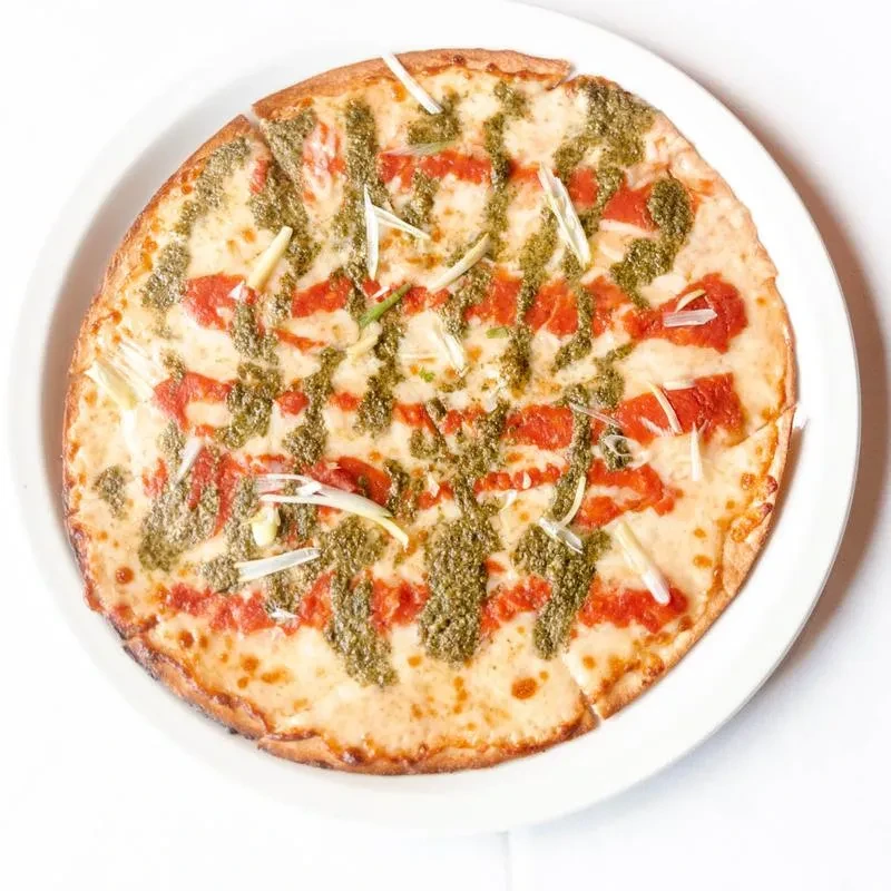 Golden crust pizza with cheese, red sauce, pesto, and green garnish.