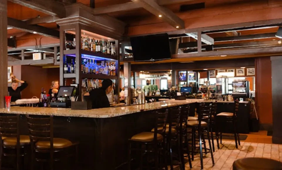 Restaurant bar with illuminated liquor bottles, dark wood, and bar stools.
