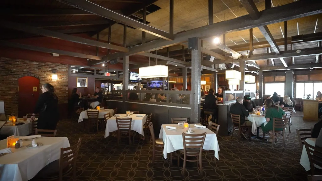 Spacious restaurant with exposed wood beams, brick, tables, and seated diners.