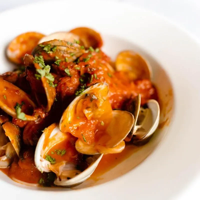 Close-up of open clams in thick tomato sauce, garnished with herbs.