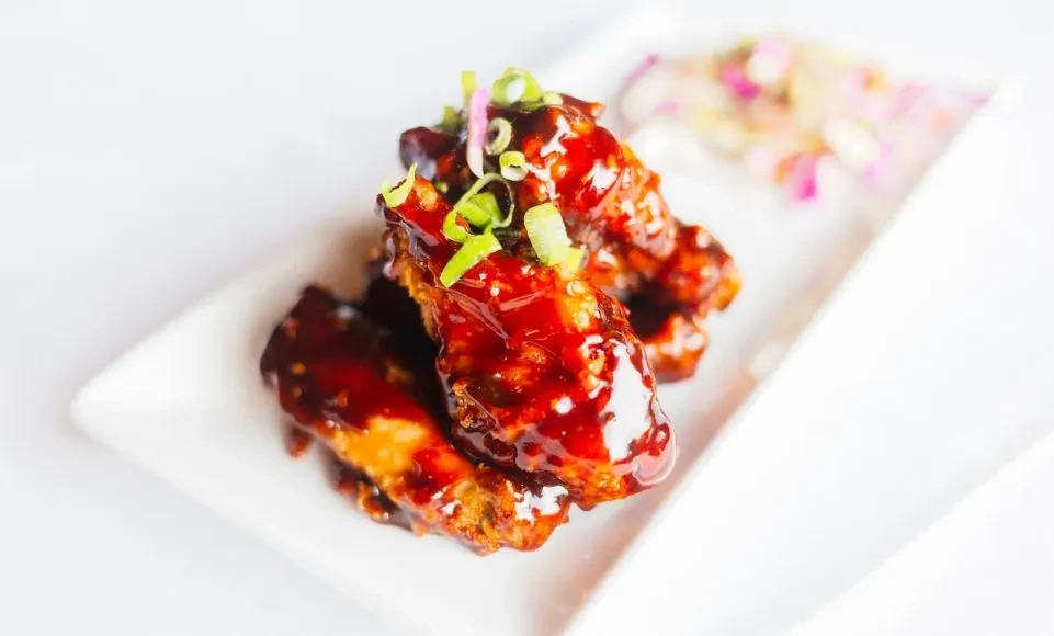 Dark red glazed chicken wings on a white plate with green onions.