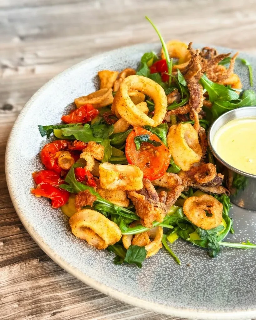 Overhead shot of fried calamari salad with greens, tomatoes, and sauce.