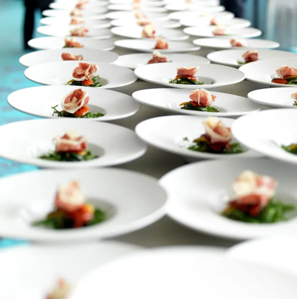 Identical canapés with prosciutto, red pepper, and greens on a long table.