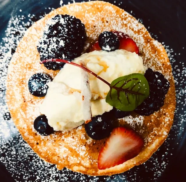 Golden pancake with mixed berries, whipped cream, powdered sugar, and mint leaf.