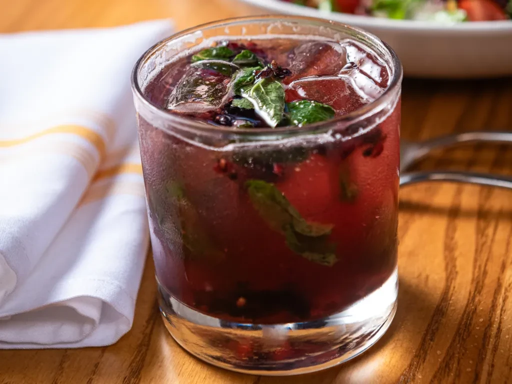Reddish-purple berry drink with ice, mint, and condensation on wood.