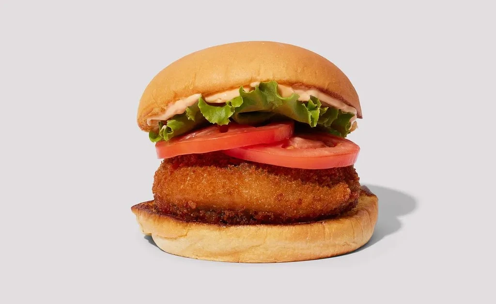 Fried patty burger with brioche bun, lettuce, tomato, and sauce.