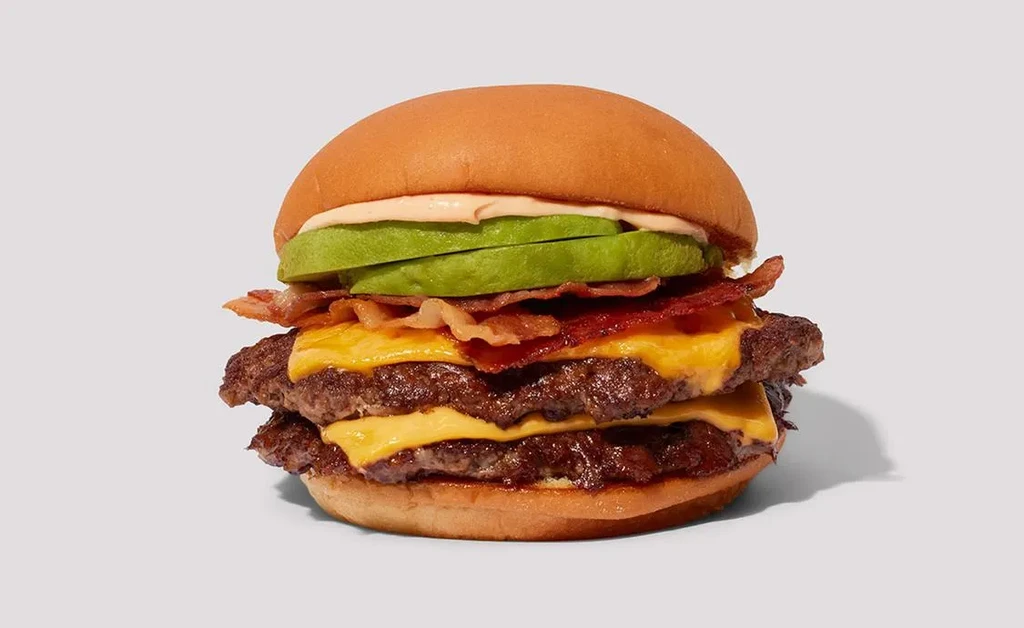 Close-up double cheeseburger with bacon, avocado, pink sauce, gray background.