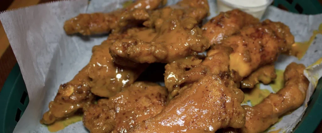 Green basket of saucy chicken wings with a ramekin of creamy dip.