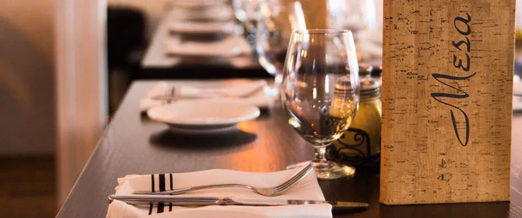 Restaurant table close-up: napkin, cutlery, wine glass, and 'Mesa' menu.