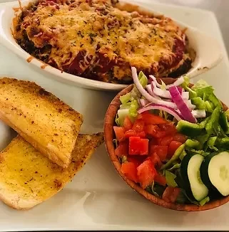 Baked casserole with red sauce, garlic bread, and vegetable salad.