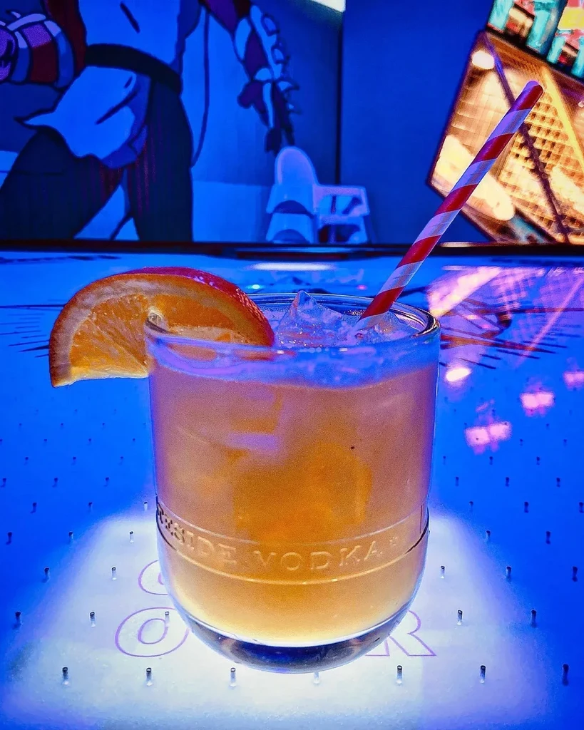 Neon-lit cocktail with orange slice, straw, and embossed text.