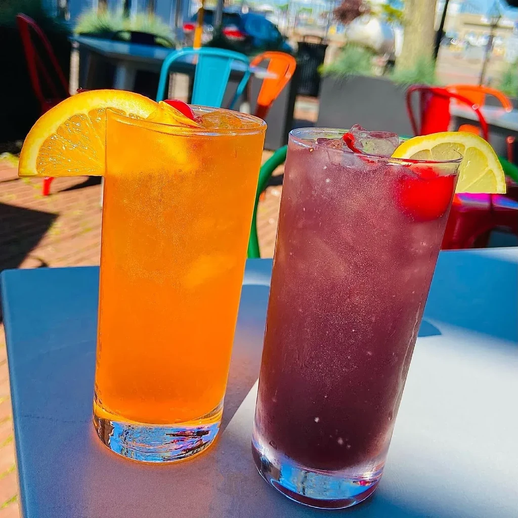 Two colorful, fruit-garnished iced drinks on an outdoor patio.