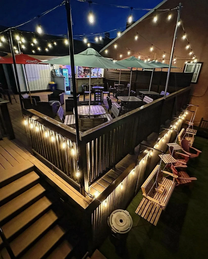 Nighttime multi-level wooden deck patio with string lights and diverse seating.