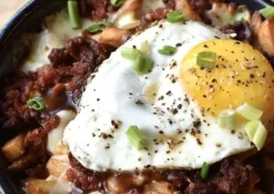 Fried egg seasoned with pepper over crumbled meat and green onions.