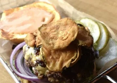 Overhead open-faced burger with crispy toppings, cheese, pickles.