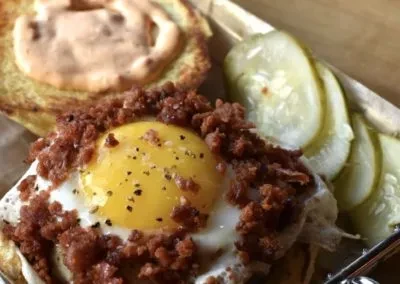 Fried egg with pepper on crumbled meat, toasted bun, and dill pickles.
