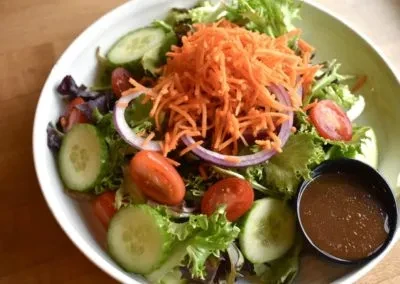 White bowl of fresh mixed salad with a side of dressing.