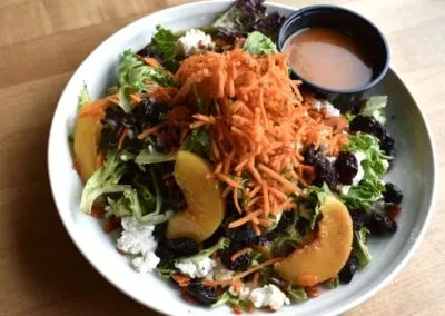 Colorful salad with greens, peaches, carrots, dried fruit, cheese, and dressing.
