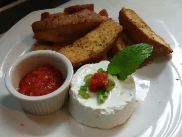 Appetizer platter with cheese, red relish, pepper spread, and toasted bread.