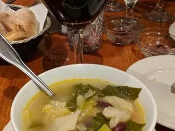 Vegetable soup, red wine, and bread on a warm restaurant table.