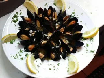 Cooked mussels with open shells, orange meat, lemon, and green herbs.