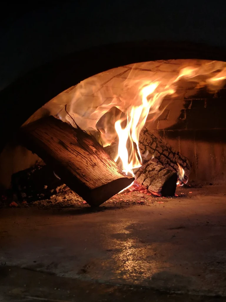 Bright orange flames and glowing embers burn inside a brick oven.